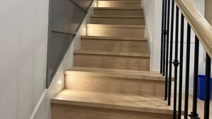 A wooden staircase with black railings and a blue trash bin at the bottom. - Pristine Brand New Duplex, Prime Location! (Vancouver)