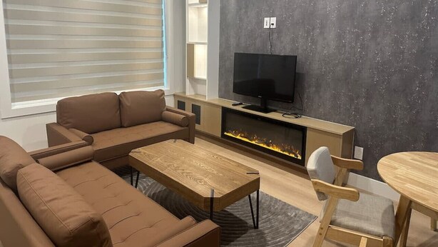 A modern living room with a sectional sofa, a wooden coffee table, a TV, and a fireplace. - Pristine Brand New Duplex, Prime Location! (Vancouver)