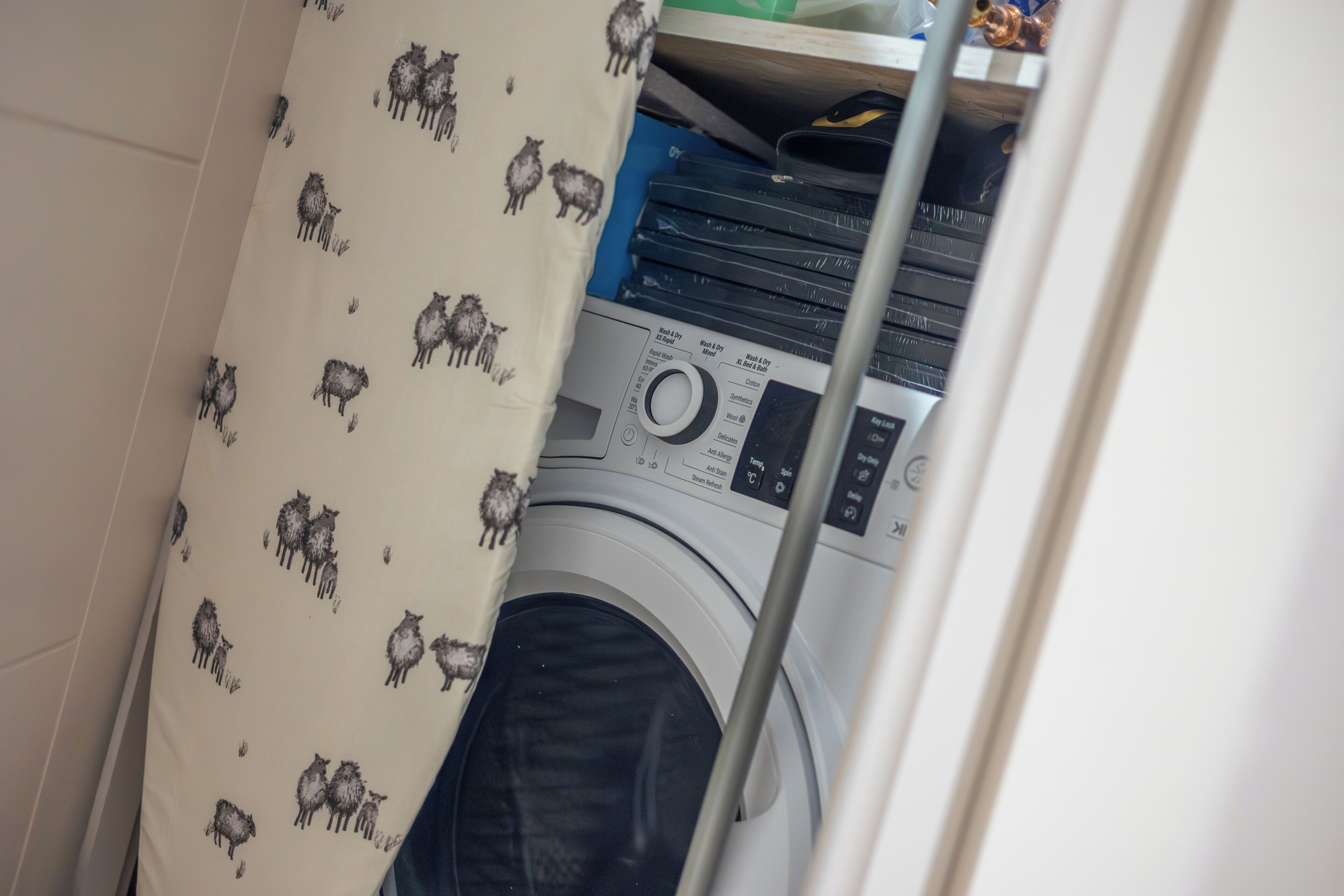 A laundry area with a washing machine, a shelf with books, and a patterned curtain.