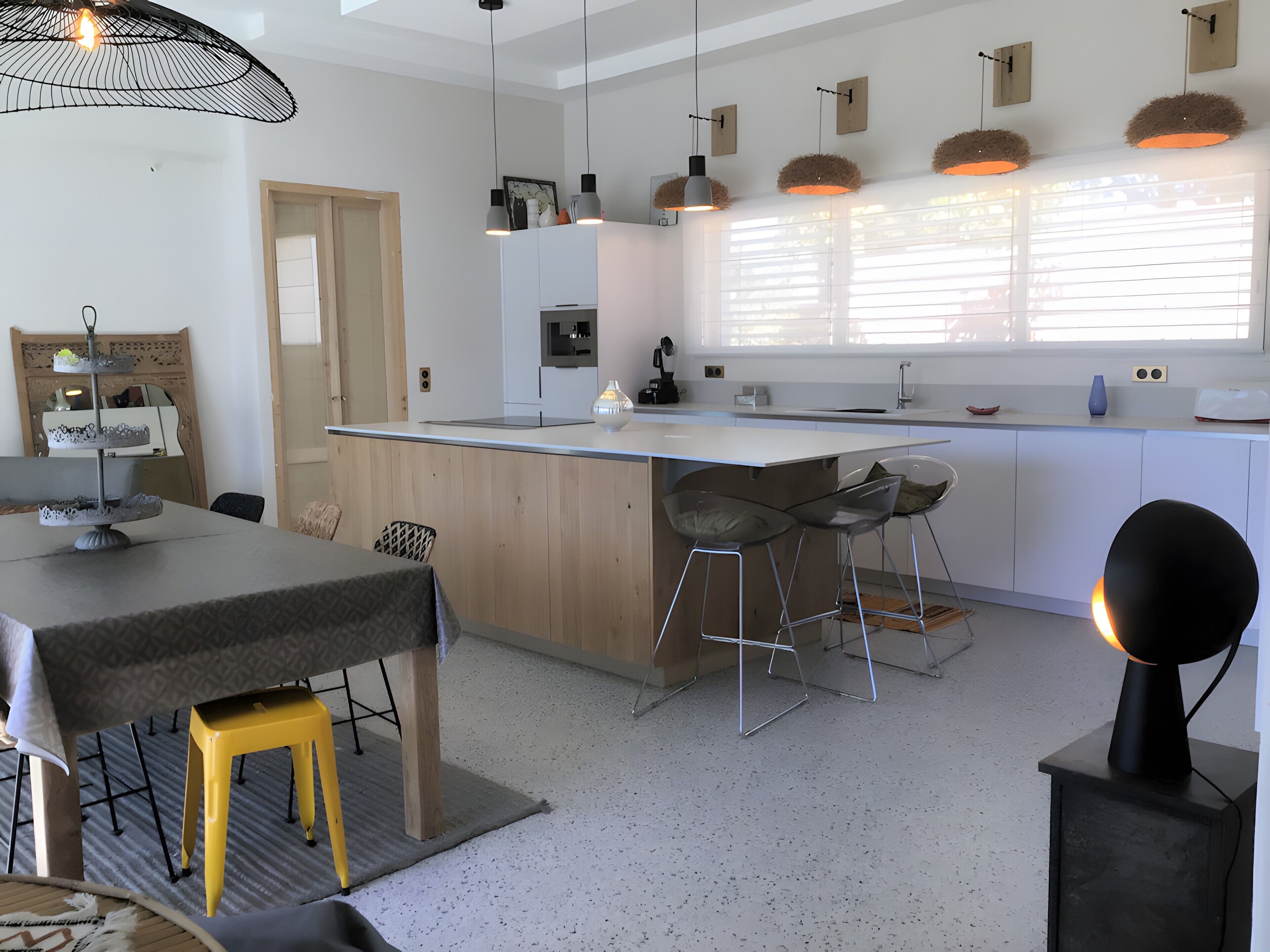 A modern kitchen with a central island, bar stools, pendant lighting, and a dining area with a table and chairs.
