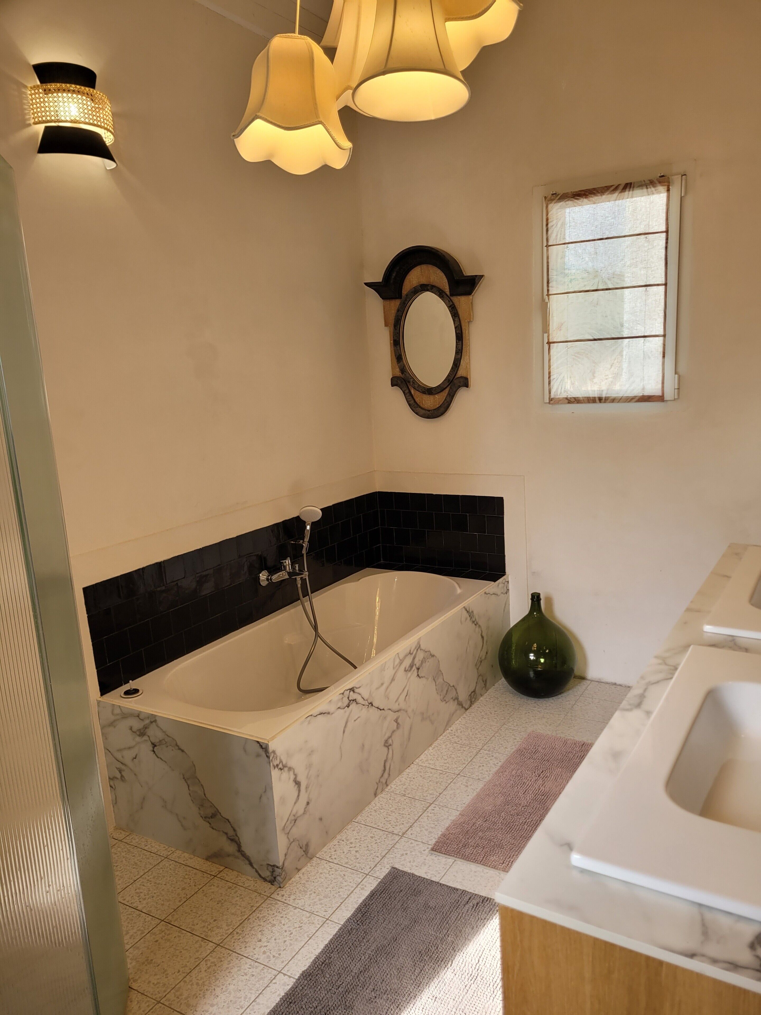 A bathroom with a bathtub, a mirror, a window, and a green bottle on the counter.