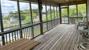 A covered outdoor deck with a view of a river, wooden benches, and a table. - OC80: Suite: Canal front with private boat dock and large yard (Ocracoke)