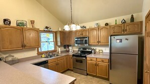 A kitchen with wooden cabinets, stainless steel appliances, and a granite countertop. - OC80: Suite: Canal front with private boat dock and large yard (Ocracoke)
