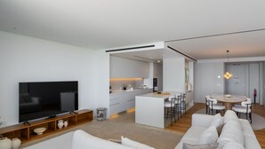 Een moderne woonkamer met een flatscreen televisie, een bank en een eethoek met een ronde tafel en stoelen.