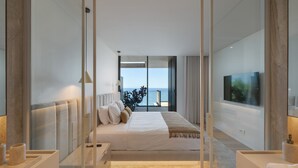Een moderne slaapkamer met een groot bed, een televisie aan de wand en uitzicht op zee door grote ramen.