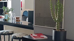 Una cocina moderna con comedor, que incluye una planta en maceta, una estantería con sombreros y un ventanal con vista a un atardecer.