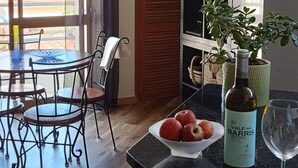 Una cocina moderna con comedor, que presenta suelo de madera, una mesa de comedor con sillas, un refrigerador, una planta en maceta y una botella de vino.