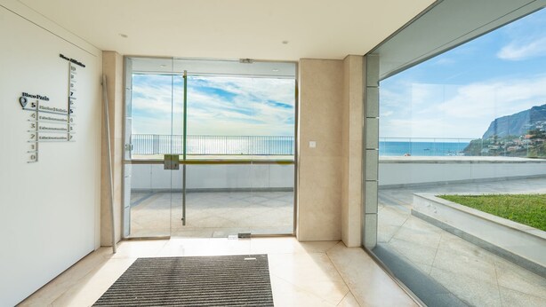 Ein moderner Hotelzugang mit einer Glastür, die zu einem Balkon mit Blick auf das Meer und ein Berg führt.