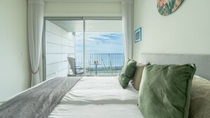 Ein Hotelzimmer mit Bett, grünen Kissen, Meerblick und einem Balkon mit Stuhl und Tisch.