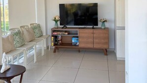 A living room with a wooden TV stand, a flat-screen TV, and a seating area with a bench and chairs.