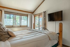 Een slaapkamer met een bed, een aan de muur bevestigde televisie en ramen met gordijnen.