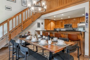A dining area with a wooden table set for four, surrounded by black chairs. A staircase with wooden railings leads to an upper level. - Shared Hot Tub and Pool | Mountain Views (Mammoth Lakes)
