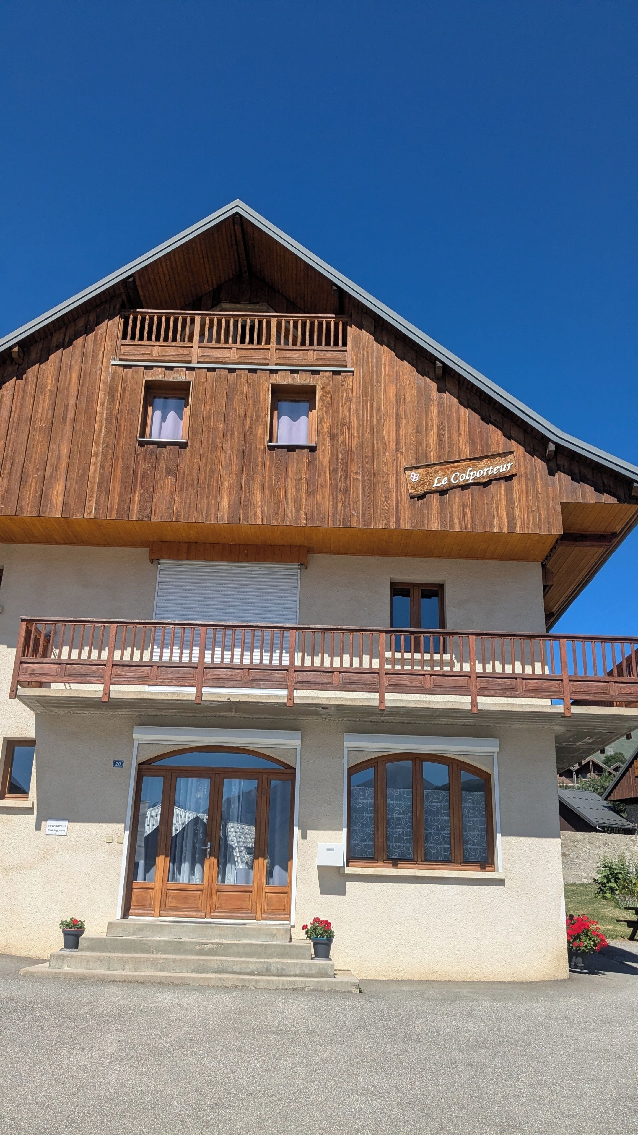 Een houten chalet met een balkon, een bord waarop 'Le Colporter' staat en een dubbele deur ingang.