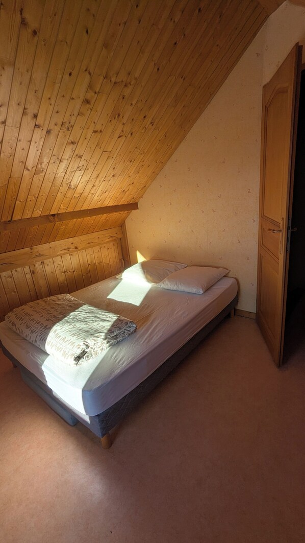 En enkeltseng i et rum med trælofter og en dør til højre.