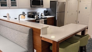 Cocina moderna con una isla central, armarios blancos, electrodomésticos de acero inoxidable y una zona de estar con banco y taburetes.