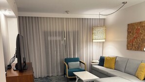 Una sala de estar moderna con un sofá seccional gris, un sillón azul, una mesa de centro blanca y una mesita de noche de madera con un televisor.