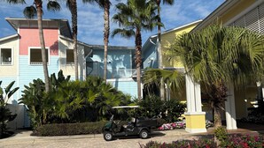 Un patio con palmeras, un carrito de golf y edificios coloridos.