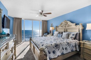 Ein Schlafzimmer mit einem großen Bett, einem Deckenventilator, Meerblick, einem Schminktisch und einer Lampe.