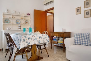 A dining area with a table set for four, a wooden chair, a bookshelf with decorative plates, and a white sofa. - Apartment 'Zaffiro  with Garage' with Private Terrace, Wi-Fi and Air Conditioning (Rapallo)