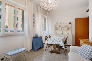 A dining area with a table, chairs, a bench, a chandelier, and a view of buildings through a window. - Apartment 'Zaffiro  with Garage' with Private Terrace, Wi-Fi and Air Conditioning (Rapallo)