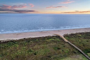 Een kustlandschap met een strand, een houten vogelbeschermingsgang en helder uitzicht op de oceaan.