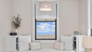 Eine gemütliche Leseecke mit einer gepolsterten Bank, einer Hängeleuchte und Blick zum Himmel durch ein Fenster.