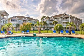 A hotel with a swimming pool, multiple balconies, and a fenced outdoor area with lounge chairs. - Chic Coastal Retreat | Pool & Golf access (Myrtle Beach)