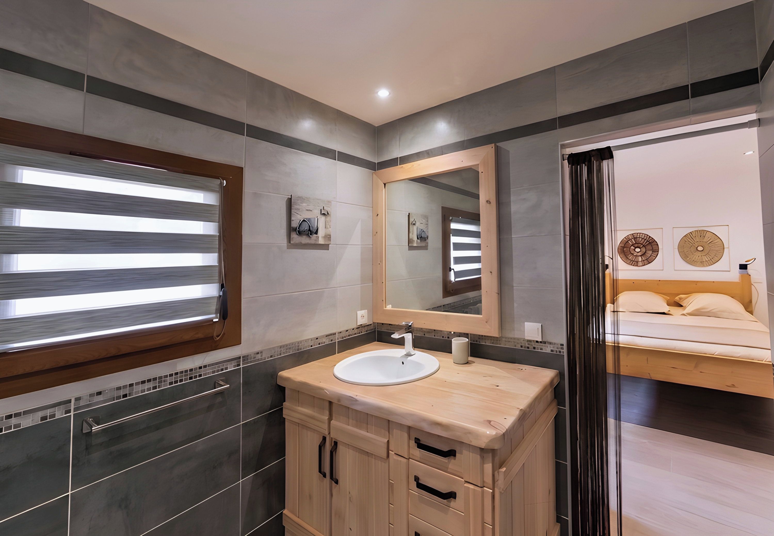 A modern bathroom with a wooden vanity, a large mirror, and a view into the bedroom.