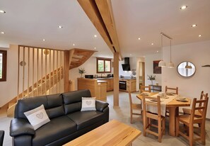 Ein modernes Interieur mit einem schwarzen Ledersofa, einem Holzes Esstisch und einer Treppe mit Holzhandläufen.