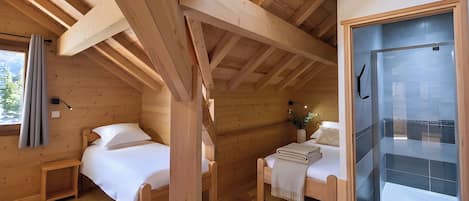 Eine Holz-Blockhütte mit zwei Betten, einem Dachfenster und einer Glasdusche.