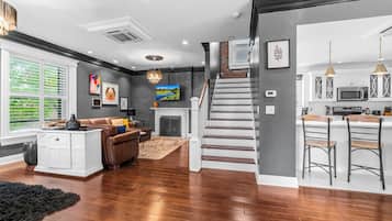 A modern interior with a staircase, a living area with a fireplace, and a kitchen with bar stools.