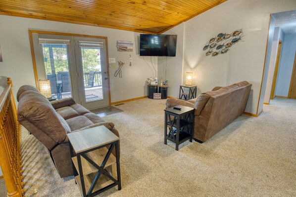 A living room with a brown sofa, a small table, a TV mounted on the wall, and a door leading to a balcony.