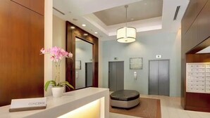 Un área de recepción con mostrador, una orquídea en maceta, un espacio de espera circular y dos ascensores.