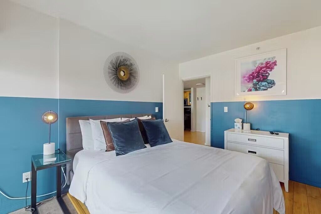 A bedroom with a bed, bedside tables, a wall clock, and a framed picture.