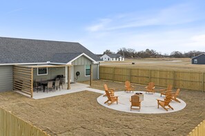 Ein Garten mit überdachter Terrasse, Sitzgelegenheiten im Freien und einem Sandbereich.