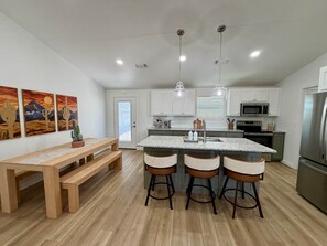 Une cuisine moderne dotée d’un îlot central, de tabourets de bar, d’un banc en bois et de luminaires suspendus.