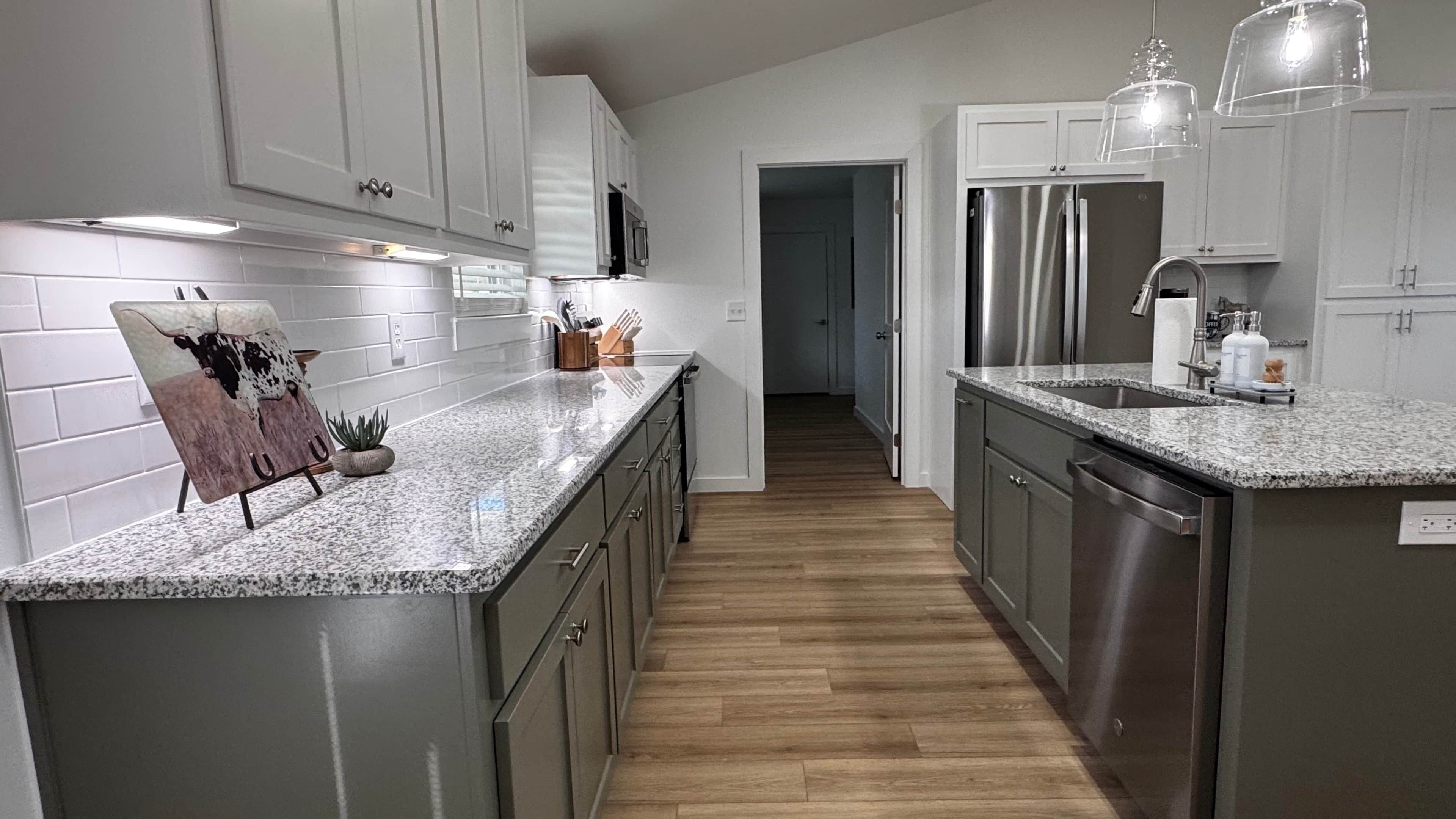 A modern kitchen with granite countertops, stainless steel appliances, and a wooden floor.