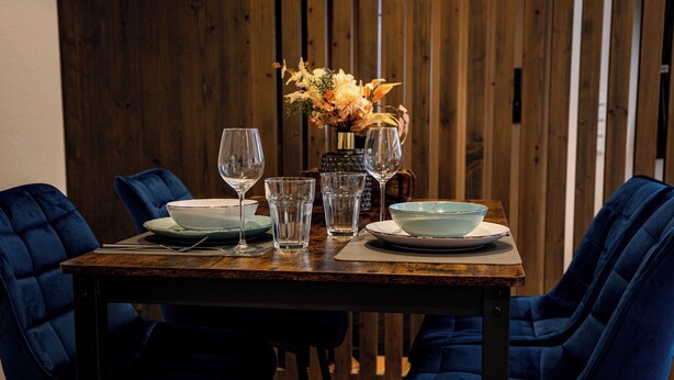 A dining table set with plates, glasses, and a vase of flowers. - 24-7 Apartment Passau - Ferienwohnung (Passau)