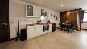 A modern kitchen with white cabinets, a built-in oven, and a dining area with a table and chairs. - 24-7 Apartment Passau - Ferienwohnung (Passau)