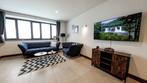 A modern living room with a large TV, a sofa, a coffee table, and a rug. - 24-7 Apartment Passau - Ferienwohnung (Passau)