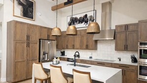A modern kitchen with wooden cabinets, a stainless steel refrigerator, a large island with bar stools, pendant lights, and a black faucet. - Upscale ski-in ski-out residence, Walk to Village & Gondola, Hot tub Access (Keystone)