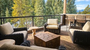 A covered outdoor seating area with wicker furniture, a round wooden table, and a view of trees and mountains. - Upscale ski-in ski-out residence, Walk to Village & Gondola, Hot tub Access (Keystone)