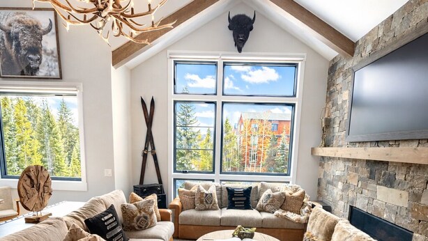A spacious living room with a high ceiling, a large fireplace, a stone wall, and a large window overlooking a forest. - Upscale ski-in ski-out residence, Walk to Village & Gondola, Hot tub Access (Keystone)