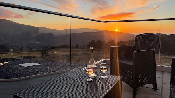 A balcony with a table set for two, overlooking a scenic landscape with a sunset view. - Groeslon Uchaf (Caernarfon)
