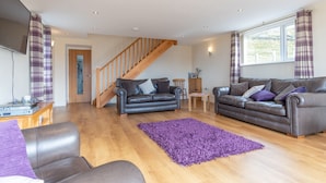 A spacious living room with two leather sofas, a wooden staircase, and a large window with curtains. - Groeslon Uchaf (Caernarfon)