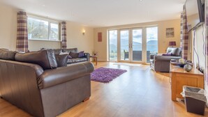 A spacious living room with a brown leather sofa, a grey sofa, and a wooden coffee table. There is a purple rug on the floor, and a TV mounted on the wall. - Groeslon Uchaf (Caernarfon)