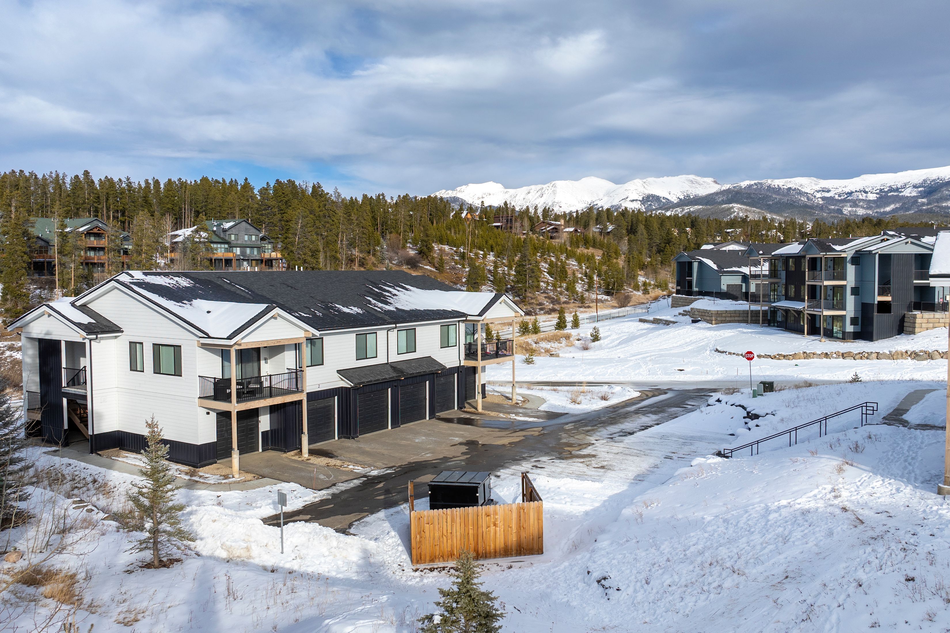 A modern residential area with multi-story houses, a snow-covered landscape, and mountains in the background.