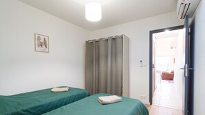 Ein Zimmer mit zwei Betten, einem Vorhang, einer Tür zu einem anderen Raum und einem gerahmten Bild an der Wand.