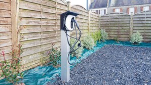 Eine Ladestation für Elektroautos in einem Gartenbereich mit Holzzaun und Kiesweg.