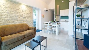 Ein modernes Wohnzimmer mit Steinwand, einem braunen Sofa, einem Esstisch mit Stühlen und einer Küchenzeile mit weißen Schränken.